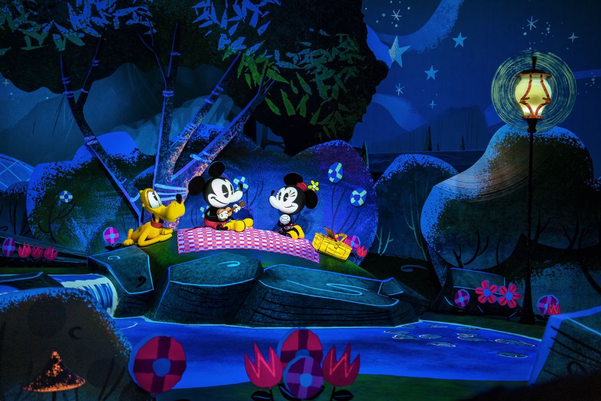 Scene from Mickey & Minnie’s Runaway Railway featuring Mickey, Minnie, and Pluto having a nighttime picnic in a colorful cartoon landscape with glowing stars, stylized trees, and a stream nearby.