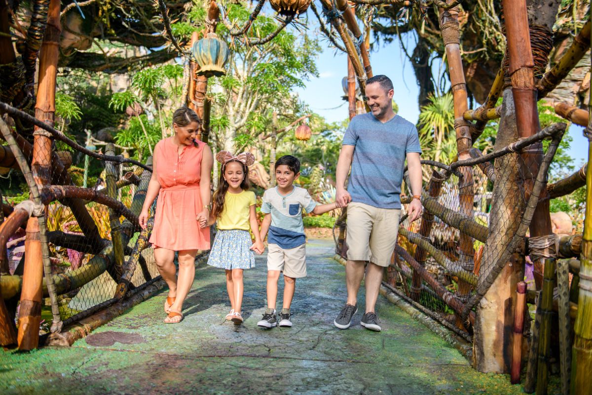 A family of four walks together through Pandora, The World of Avatar at Disney's Animal Kingdom, surrounded by lush tropical landscaping and floating mountains in the background.