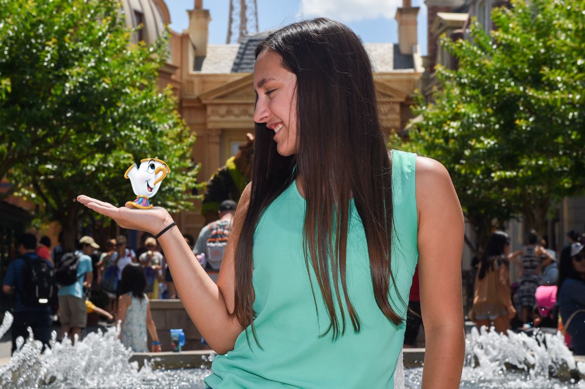A woman smiles as a digitally added Chip character from Beauty and the Beast appears to sit on her outstretched hand in a Disney PhotoPass Magic Shot at EPCOT.