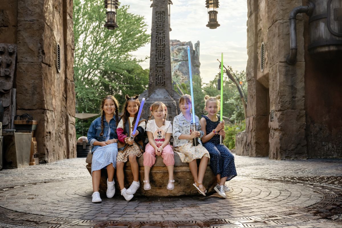 Four girls holding custom-built lightsabers in Star Wars: Galaxy's Edge at Disney's Hollywood Studios, smiling together on the stone steps of Batuu.
