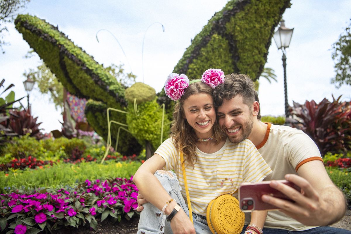 Couple taking a selfie together surrounded by colorful flowers and topiaries at EPCOT during the International Flower & Garden Festival.