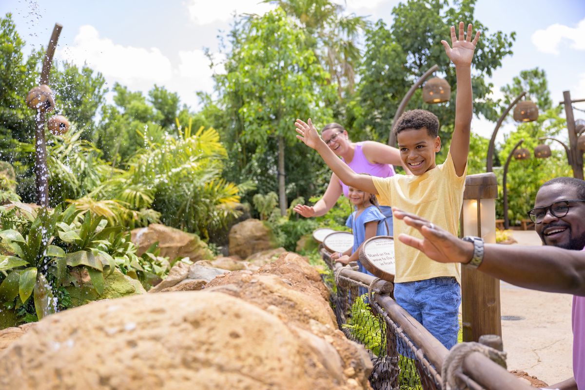A family walks along a lush, tropical pathway at Journey of Water, Inspired by Moana, at EPCOT, surrounded by greenery and flowing water features.