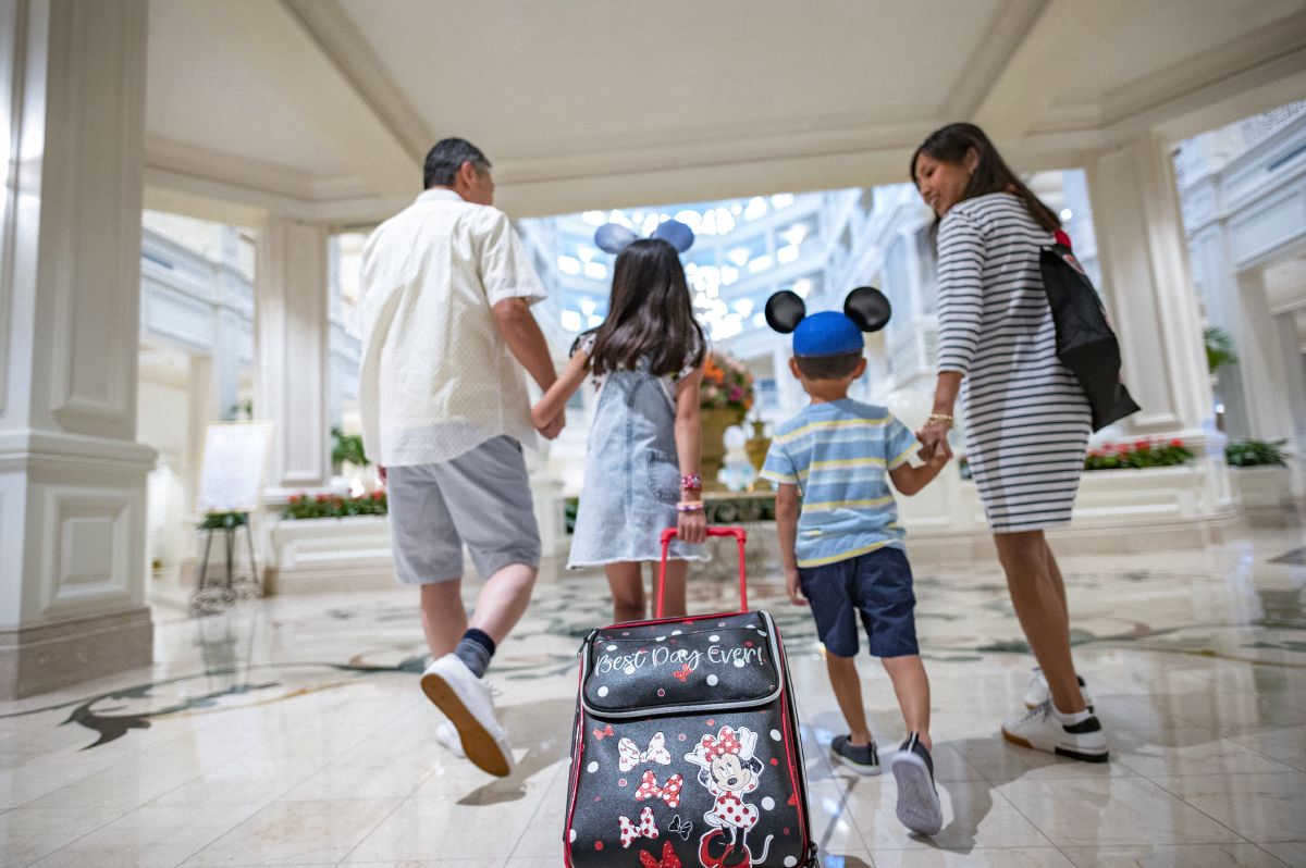 A family walks through the lobby of Disney's Grand Floridian Resort and Spa, with a child in Mickey ears pulling a Disney suitcase.