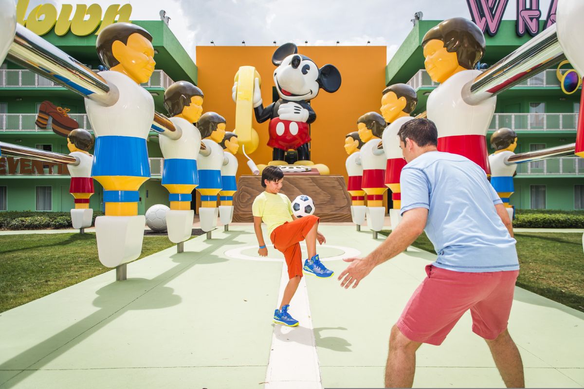 A father and child playing in the oversized foosball court at Disney's Pop Century Resort, surrounded by colorful larger-than-life character statues.