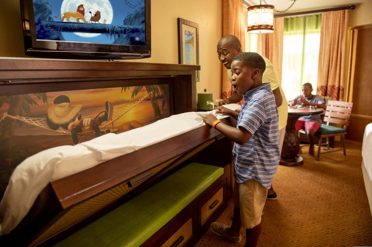 A father and son sitting together on a bed in a Disney's Caribbean Beach Resort room, enjoying a relaxed moment during their Walt Disney World vacation.
